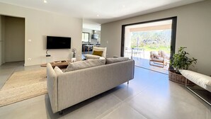 A modern living room with a large sofa, a flat-screen TV mounted on the wall, and a sliding glass door leading to a patio area. - Big house  with garden (Sotta)