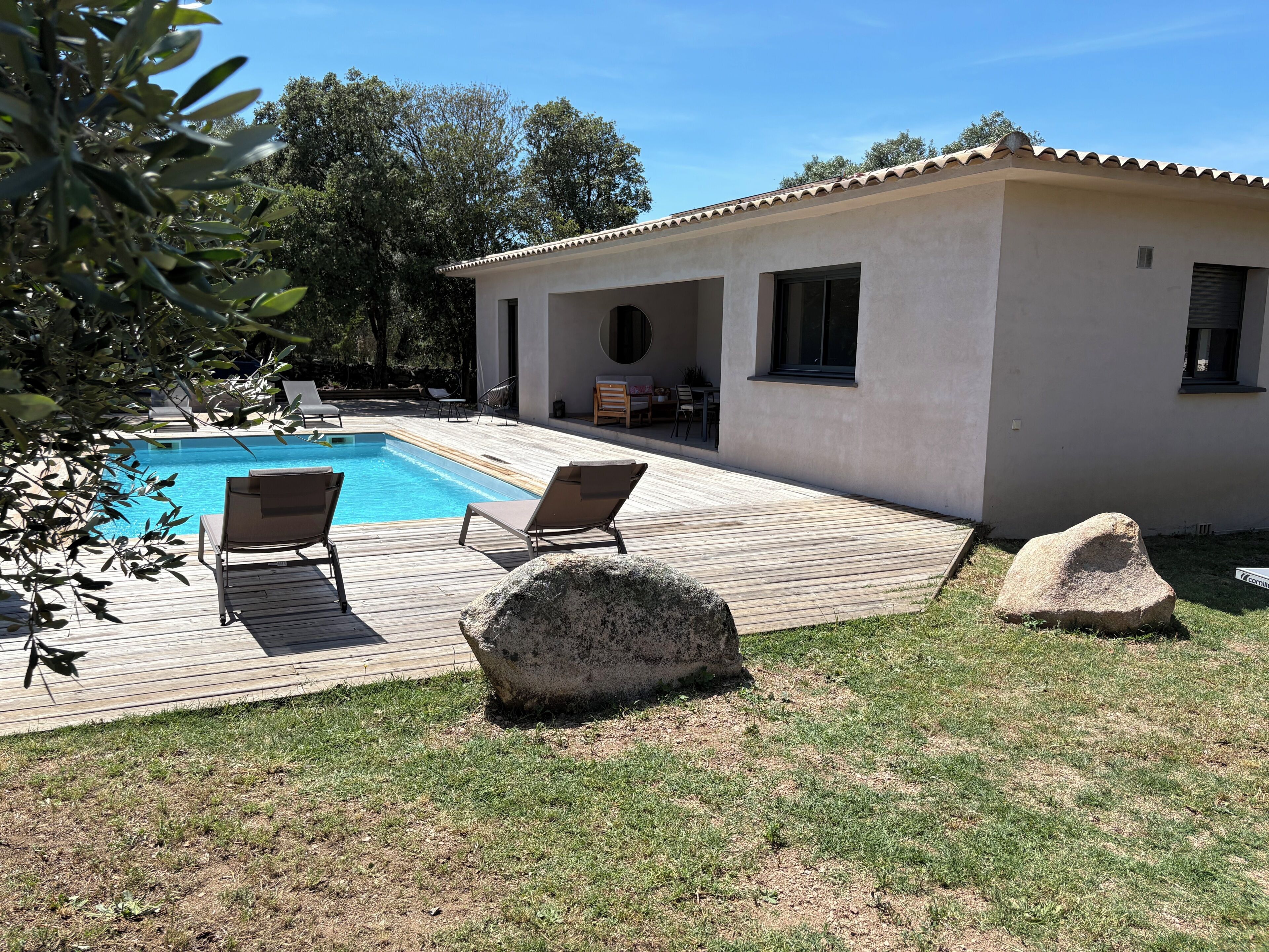Uma piscina com espreguiçadeiras, um alpendre e um edifício com telhado em azulejos.