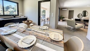 A modern dining area with a long table set for six, a kitchen with a sink and window, and a living area with a sofa and chairs. - Big house  with garden (Sotta)
