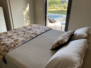 Ein Schlafzimmer mit einem Bett, Blick auf einen Pool und einem Stuhl in der Nähe des Fensters.