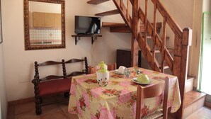 A dining area with a wooden bench, a table with a floral tablecloth, a television on a shelf, and a wooden staircase. - Brigitte, centre, 5 minutes walk to the beach, 10 minutes walk trainstation. (Tropea)