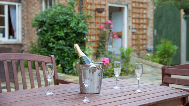 A wooden table with a metal bucket containing a bottle of champagne and two empty glasses. - The Grange Manor House, Norfolk – sleeps 30, perfect for large gatherings (Setchey)