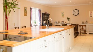 A modern kitchen with a central island, white cabinetry, and a large window with curtains. - The Grange Manor House, Norfolk – sleeps 30, perfect for large gatherings (Setchey)