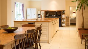 A modern kitchen with wooden cabinetry, a large island, and a dining area with a wooden table and chairs. - The Grange Manor House, Norfolk – sleeps 30, perfect for large gatherings (Setchey)