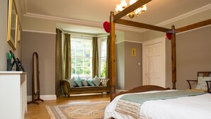 A bedroom with a four-poster bed, a sitting area with a bench and cushions, a large window with curtains, and a wooden floor. - The Grange Manor House, Norfolk – sleeps 30, perfect for large gatherings (Setchey)