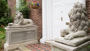 Two stone lion statues in a courtyard with a brick building and a white door in the background. - The Grange Manor House, Norfolk – sleeps 30, perfect for large gatherings (Setchey)