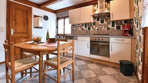 Een keuken met een houten eettafel, stoelen, een fornuis, oven en kastjes.