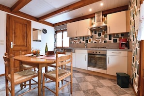 A kitchen with a wooden dining table, chairs, a stove, oven, and cabinets.