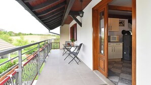 Een balkon met een tafel en stoelen, uitzicht op het landschap, en een keukenhoek met kasten en een magnetron.