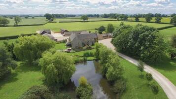 A rural estate with a pond, a pathway, and a large house surrounded by fields and trees.