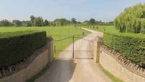 A rural road leading to a gated entrance surrounded by stone walls and hedges. - The Cotswold Manor Byre, Exclusive Hot Tub, Games Barn, 70 acres of Parkland (Bampton)