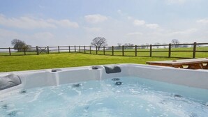 A hot tub in a grassy outdoor area with a wooden fence and picnic table in the background. - The Cotswold Manor Byre, Exclusive Hot Tub, Games Barn, 70 acres of Parkland (Bampton)