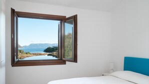 A bedroom with a large window offering a view of a lake and mountains. - Villaggio Perlacea - PERLACEA 34 (Golfo Aranci)
