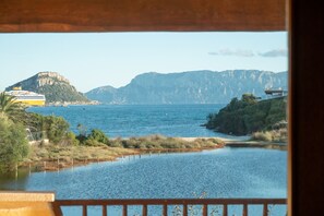 A coastal view with a ferry, a calm body of water, and mountainous terrain in the background.