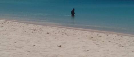 A beach with clear turquoise water and a few sailboats in the distance.