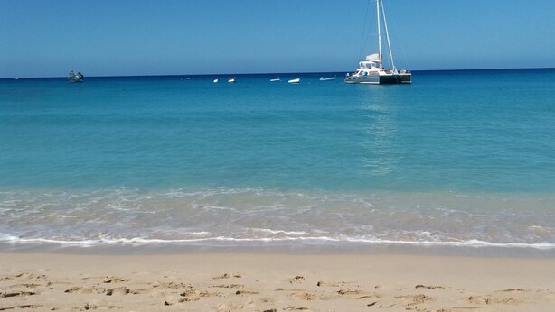 Ein Strand mit Segelboot im Wasser, blauem Himmel und sandigem Ufer.