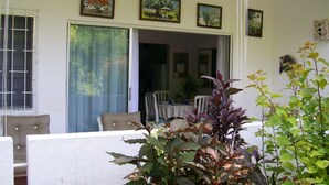 Ein Zimmer mit Esstisch und Stühlen, einer Glastür, die zu einem Außenbereich führt, und mehreren gerahmten Bildern an der Wand.