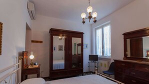 A bedroom with a bed, a dresser, a mirror, a television, and a window with curtains.