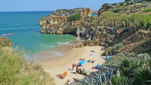 Une plage bordée d’une eau turquoise et limpide, de falaises rocheuses et d’une végétation clairsemée.