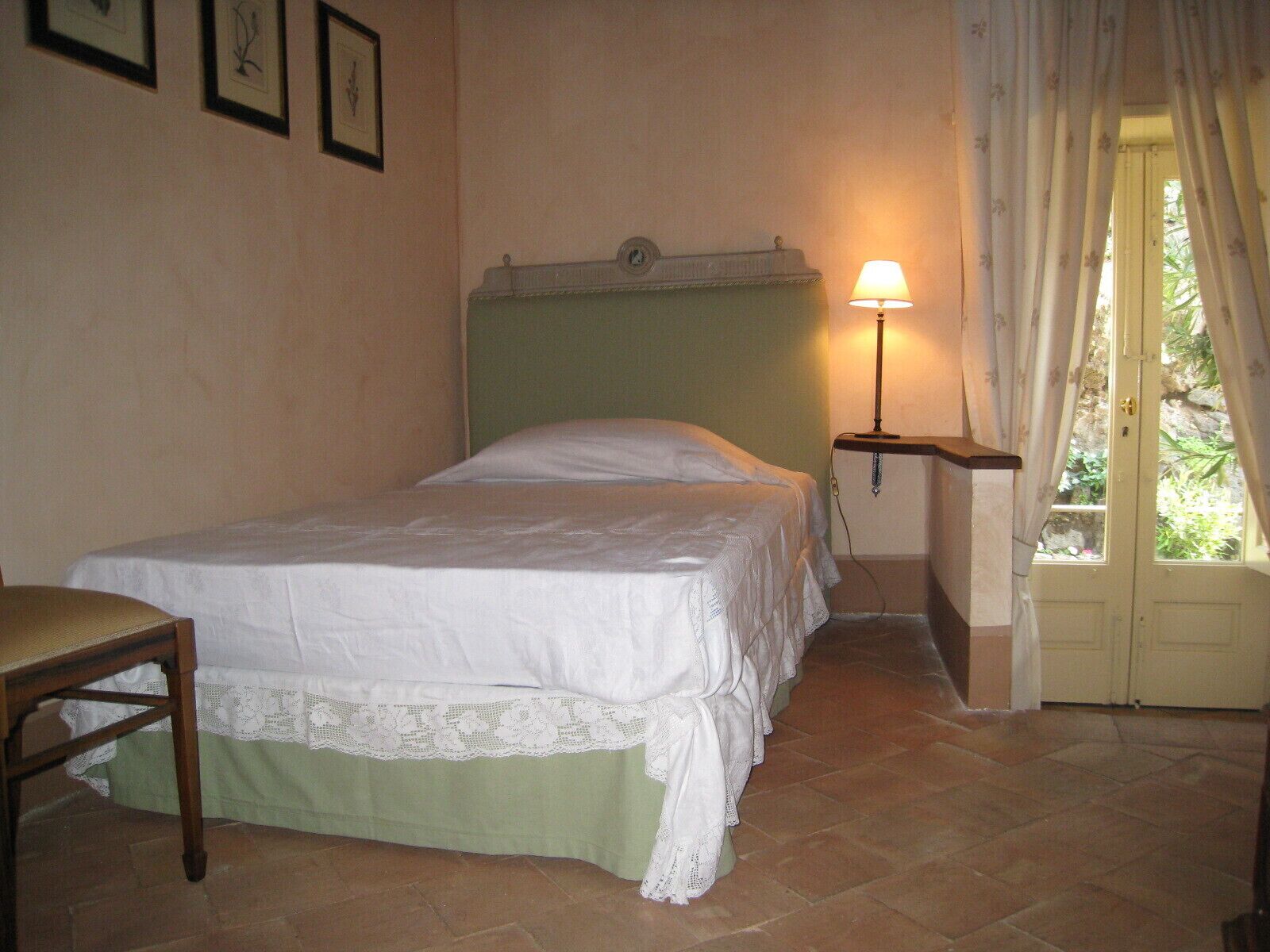 Une chambre à coucher comprenant un lit, une chaise, une table de chevet avec une lampe et une porte donnant sur un espace extérieur.