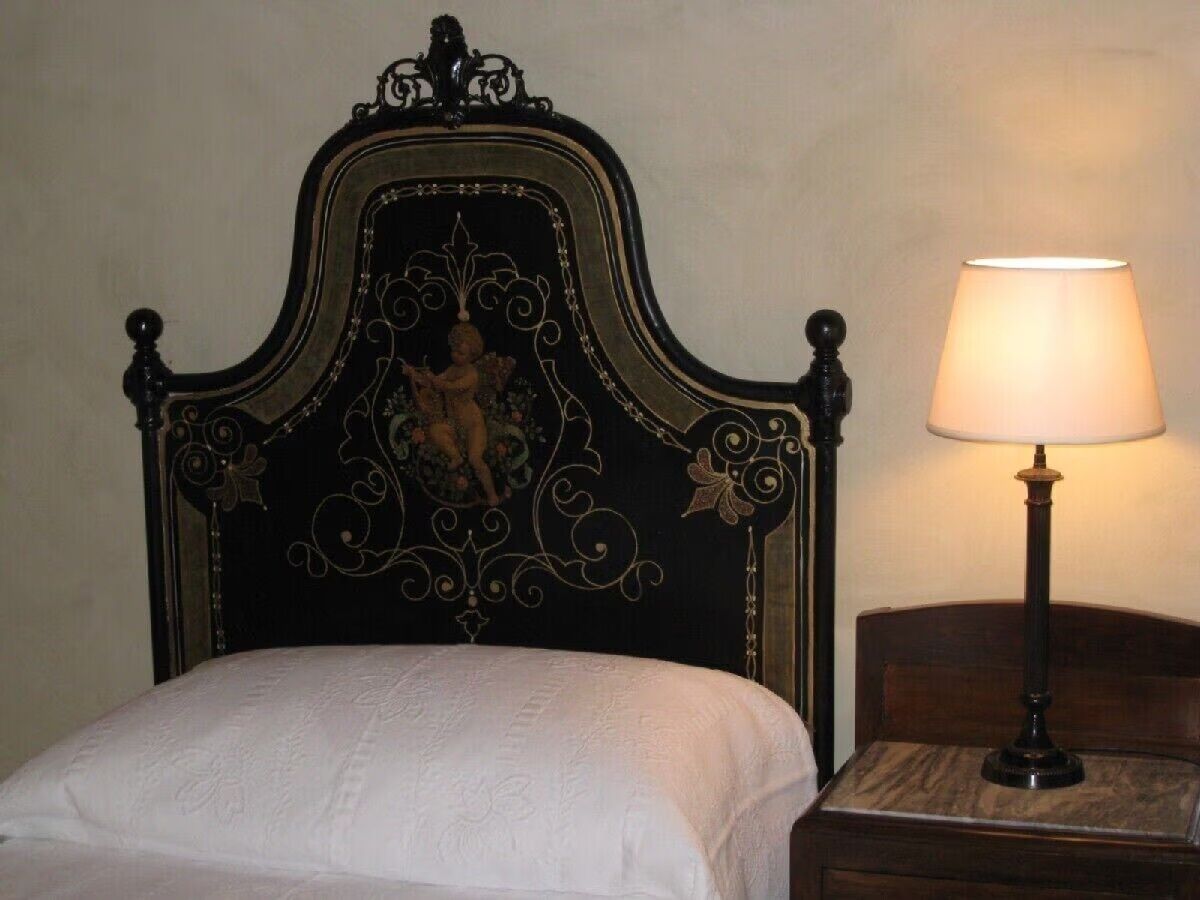 A bed with a dark headboard featuring a decorative design and a bedside table with a lamp.
