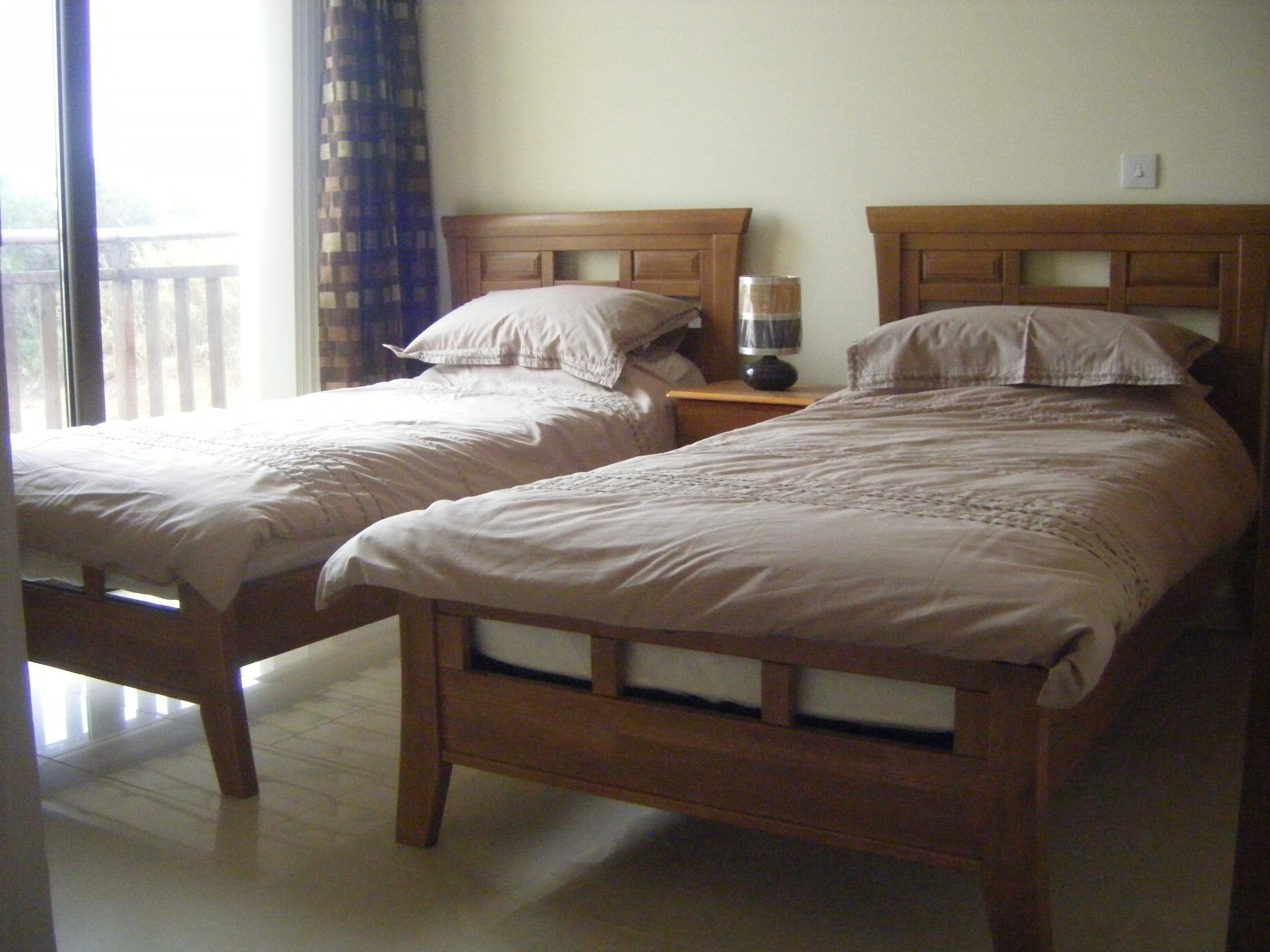 Dos camas de madera con ropa blanca en una habitación con balcón.
