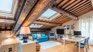 A cozy attic room with a wooden ceiling, a blue sofa, a dining table, and a TV. - Gabry's Rooftop Terrace Home with  breathtaking Views of Lucca & Tuscany (Lucca)