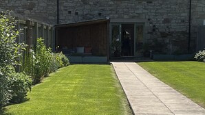 Un bâtiment en pierre doté d’un patio couvert, d’une pelouse et d’un chemin pavé.