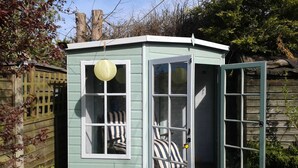 A small, light blue wooden shed with a door and windows, a striped cushion inside, and a potted plant outside. - Amber Cottage 3 Bed , In Snettisham, North Norfolk  dogs welcome (Snettisham)