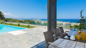 Eine Terrasse mit Pool, Esstisch, Stühlen und Blick auf das Meer und Gebäude.