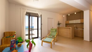 A modern living room with a view to the sea, a small kitchen, and a children's play area. - Villa Naya, walking distance to beach & sea view! (Rethymno)