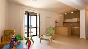 A modern living room with a view to the sea, a small kitchen, and a children's play area.
