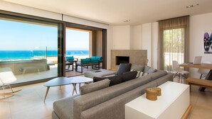 A modern living room with a large sliding glass door leading to a balcony with a view of the beach. There is a sofa, a coffee table, and a fireplace. - Villa Naya, walking distance to beach & sea view! (Rethymno)