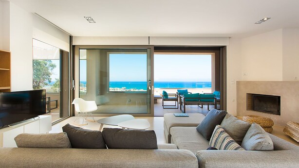 A modern living room with a large flat-screen TV, a sofa, a coffee table, and a fireplace. There is a balcony with a view of the ocean. - Villa Naya, walking distance to beach & sea view! (Rethymno)
