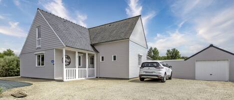 Een tweelaags huis met een overdekte veranda, een garage en een grindpad.
