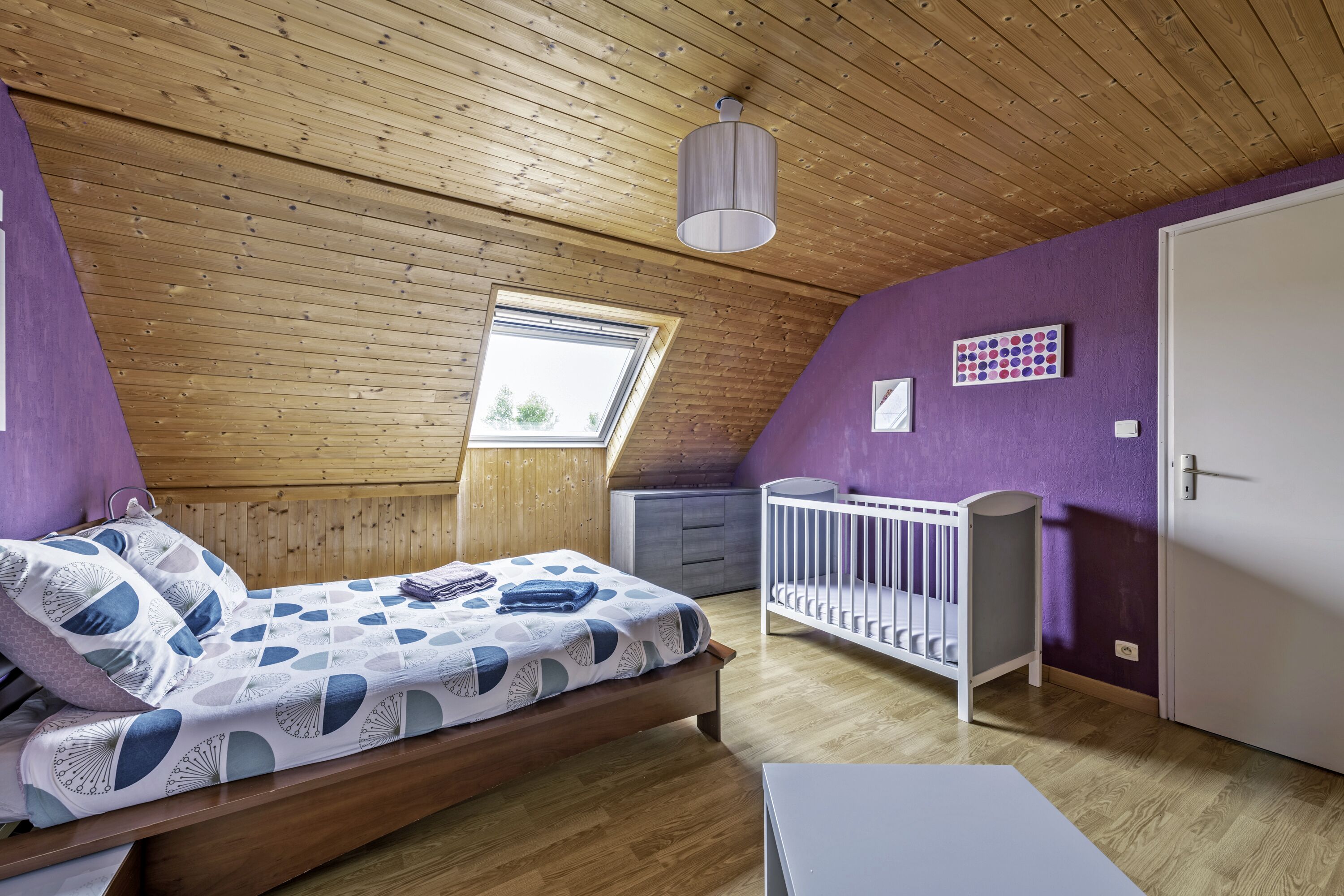Una stanza con soffitto in legno, un letto con copriletto decorato, una culla, una finestra e una porta.