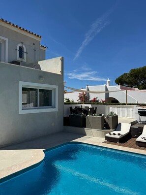 A modern house with a swimming pool, outdoor furniture, and a clear blue sky.