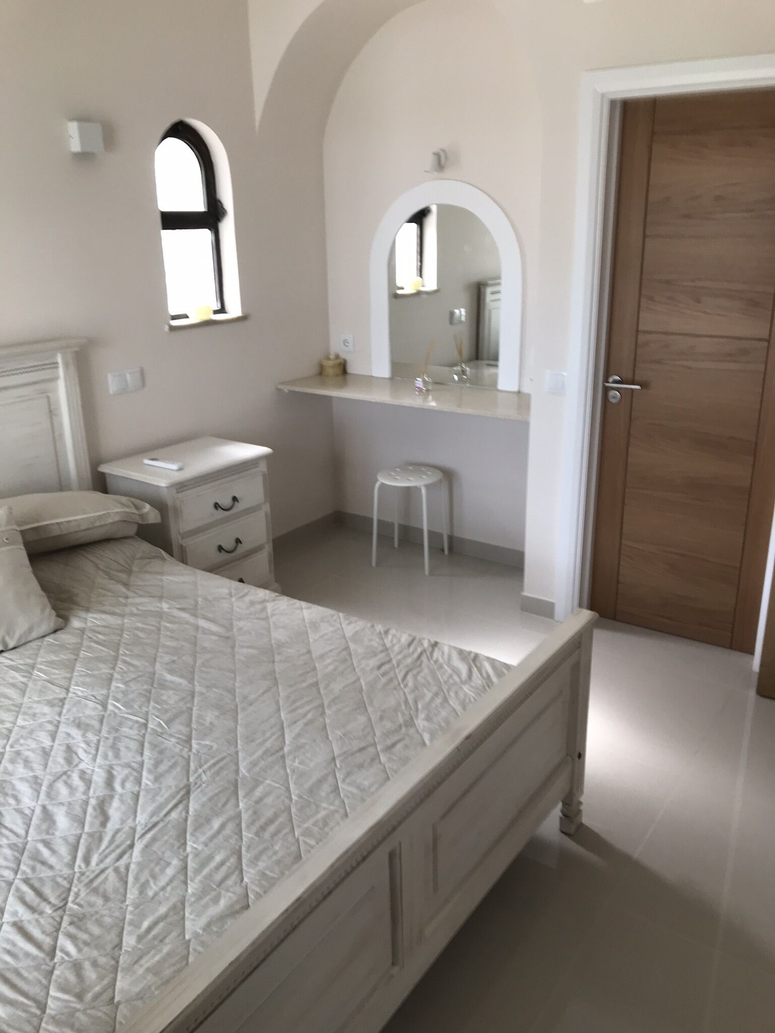 A bedroom with a bed, a nightstand, a dresser, a mirror, and a wooden door.