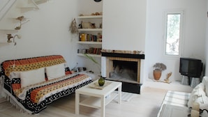 A living room with a sofa, a fireplace, a bookshelf, and a television. - Eretria: Single storey house, in an olive grove, 250 from the beach (Eretria)
