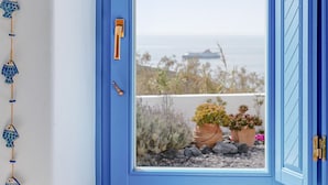 Une fenêtre à cadre bleu, offrant une vue sur un paysage côtier, avec notamment un navire et des plantes en pot.