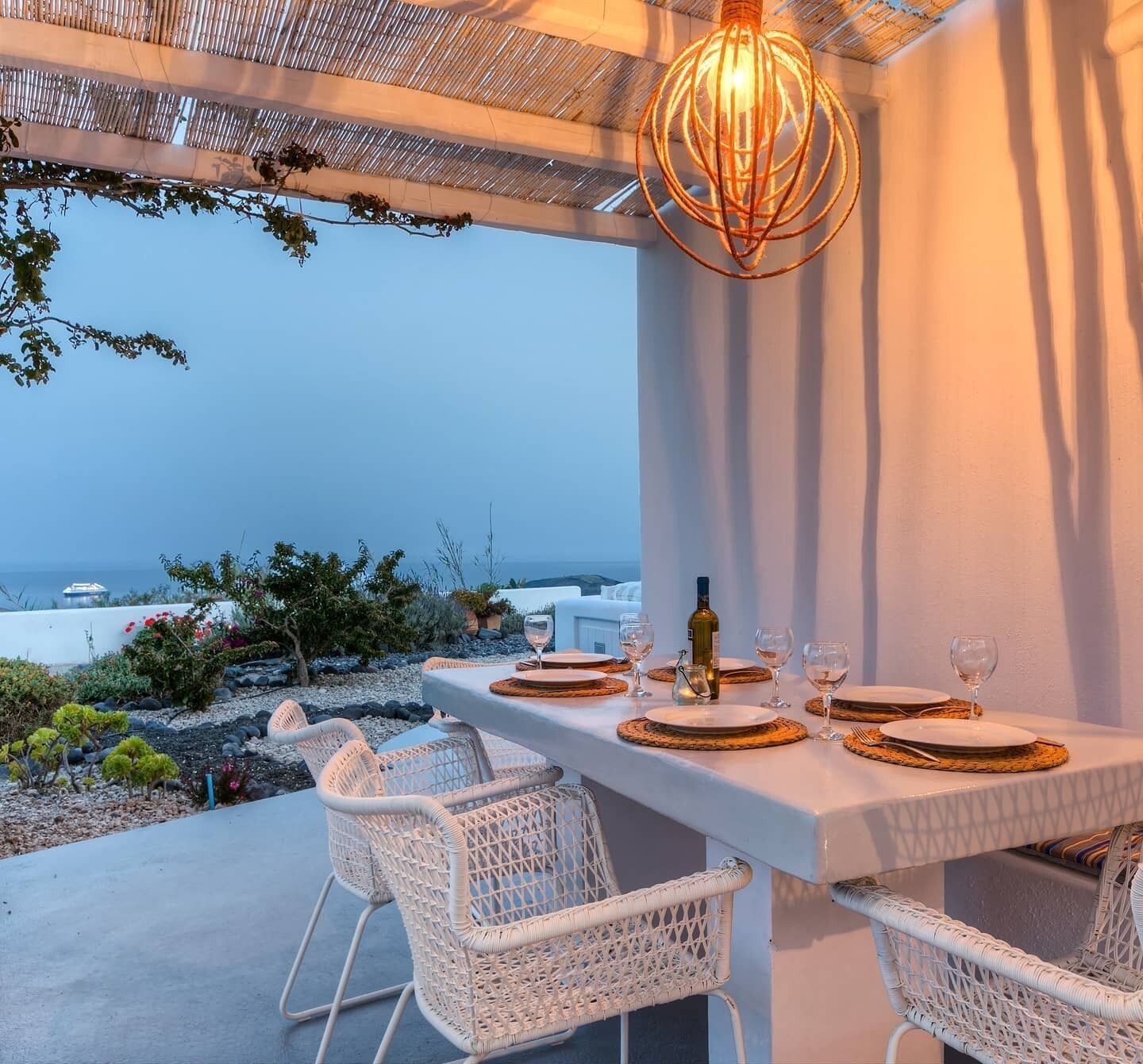 Un espace de restauration en plein air avec une table dressée pour deux personnes, offrant une vue panoramique sur la mer et les bâtiments blancs.