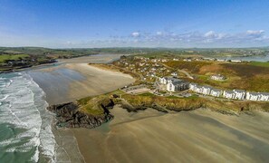 An aerial view of a coastal town with a beach, houses, and a rocky coastline.