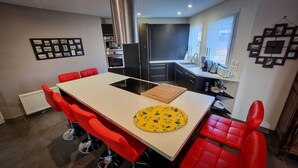 Een moderne keuken met een centraal eiland, rode stoelen en een eettafel.