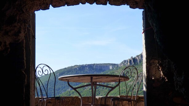 Un comedor rústico al aire libre con una mesa redonda y sillas de metal, frente a un paisaje montañoso.