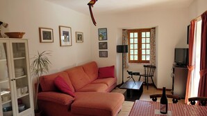 Una sala de estar con un sofá, una mesa de comedor con mantel a cuadros, un televisor y una ventana con cortinas.