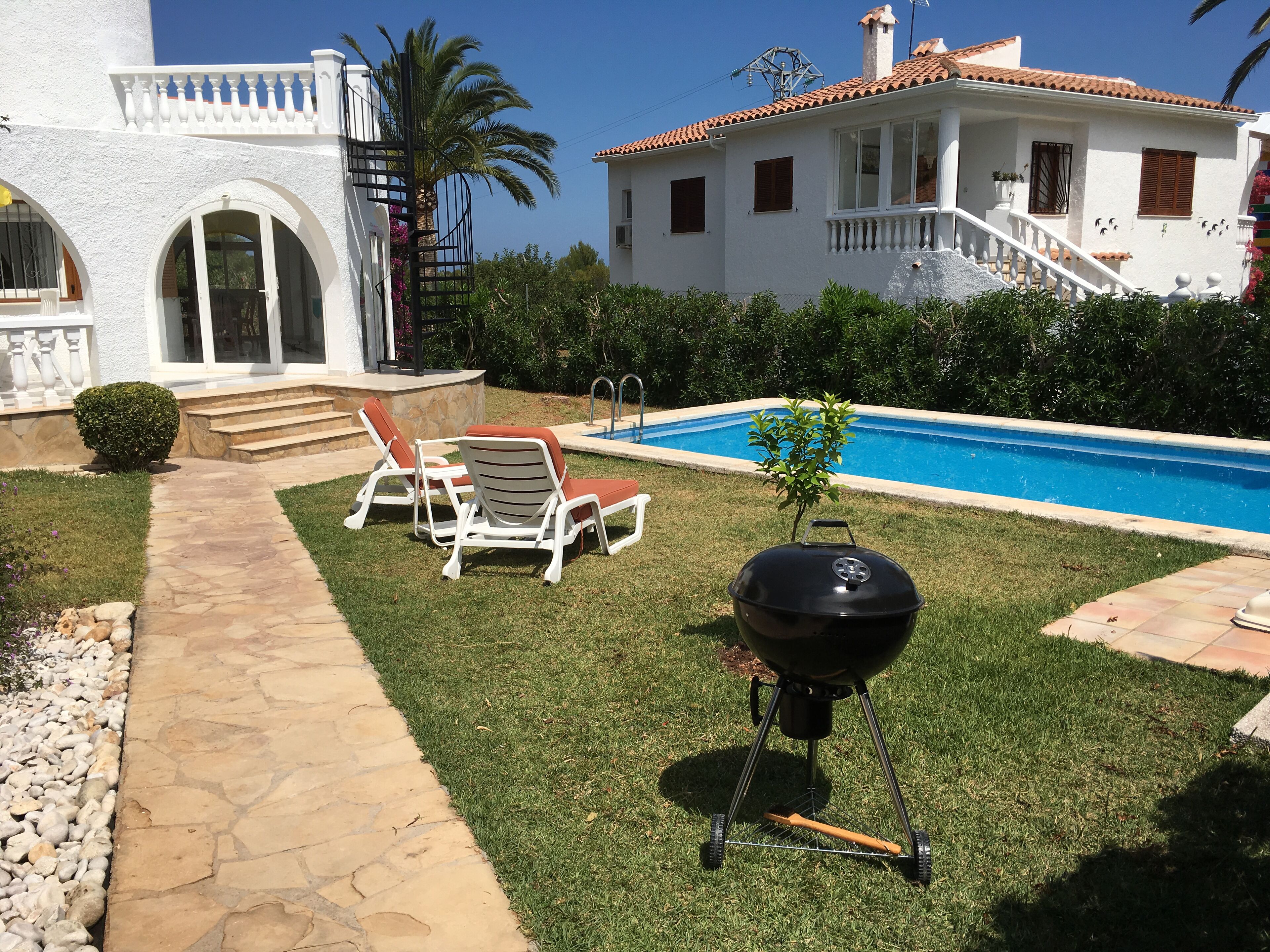 Un jardin avec une piscine, un barbecue et deux chaises longues.