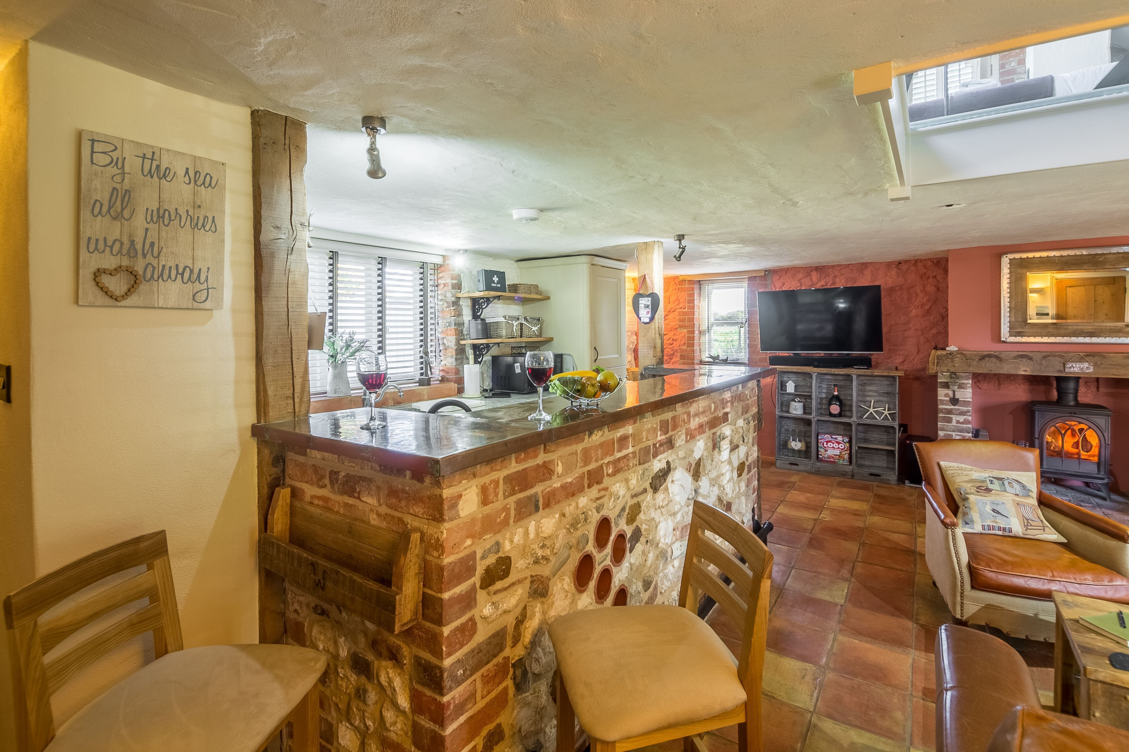 A cozy kitchen with a brick island, wooden chairs, a TV, and a fireplace.