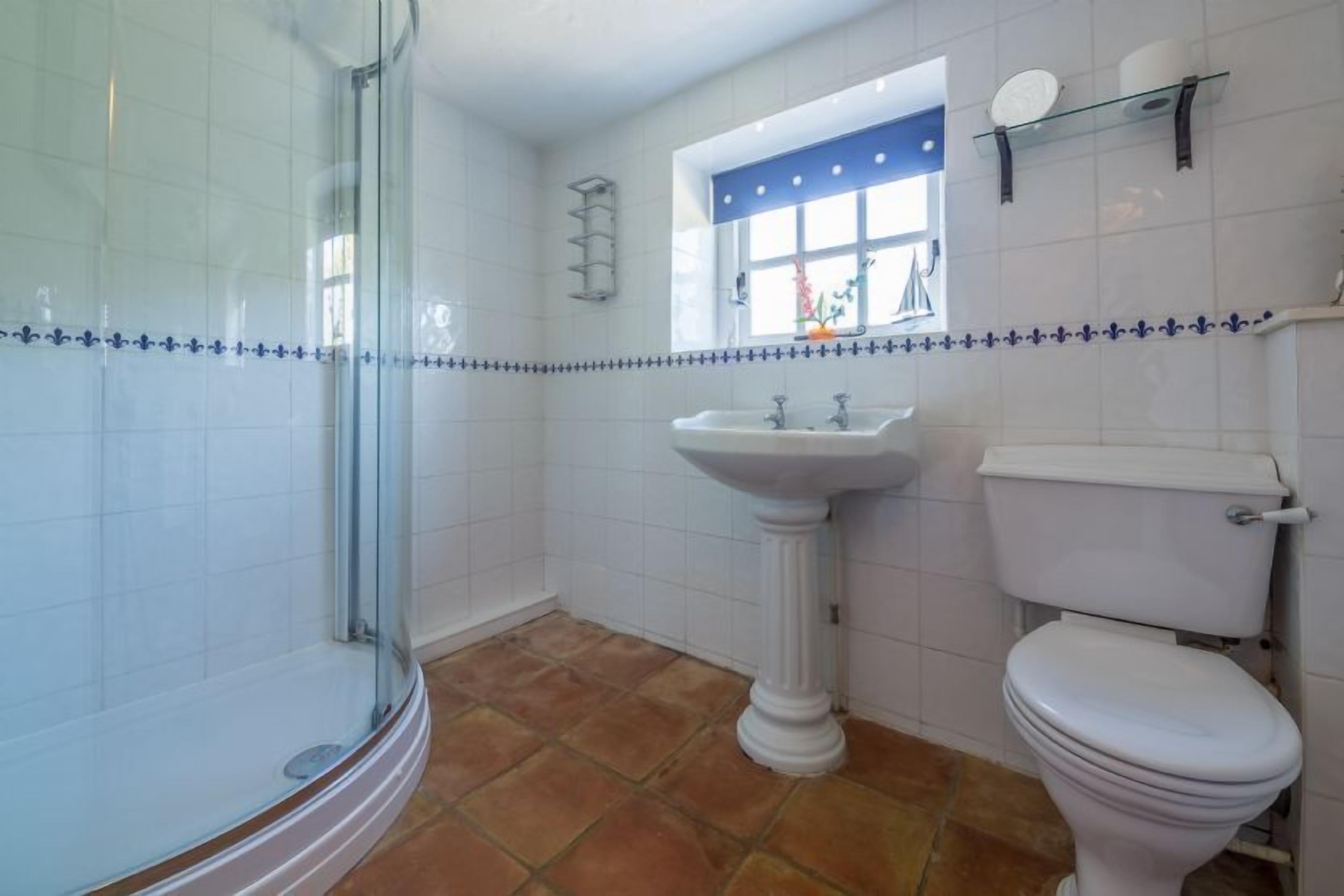 Une salle de bain avec une douche à parois de verre, un lavabo sur colonne et des toilettes.