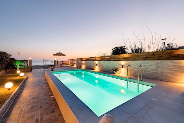 A rectangular swimming pool with a tiled deck, surrounded by a low brick wall and a wooden fence.