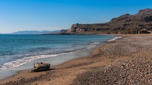 Een strand met kiezels, een rots en een berg op de achtergrond.